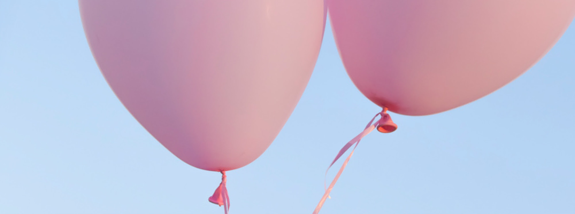 Zwei rosa Luftballons vor blauem Himmel